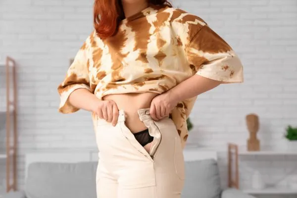 Image of woman trying to do her trousers up after pregnancy weight gain Huddersfield