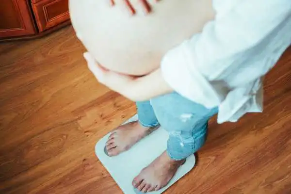 Image of woman weighing herself and experiencing weight gain through pregnancy Huddersfield